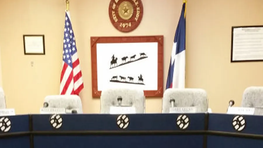 The Bruceville-Eddy council dais with the United States and Texas flags, the City seal, and a framed print of a cattle drive.