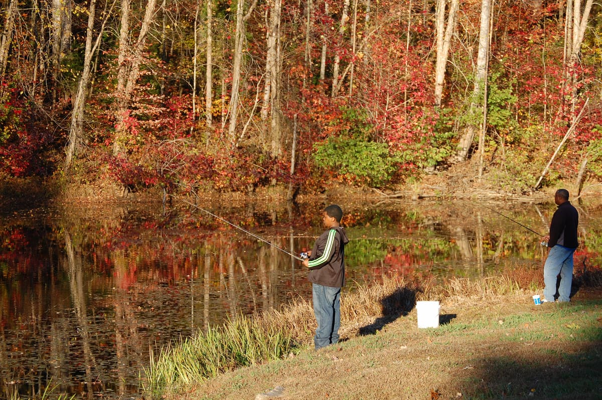 Two people fishing from the bank at Great Creek, the far bank in full autumn color and mirrored in still water