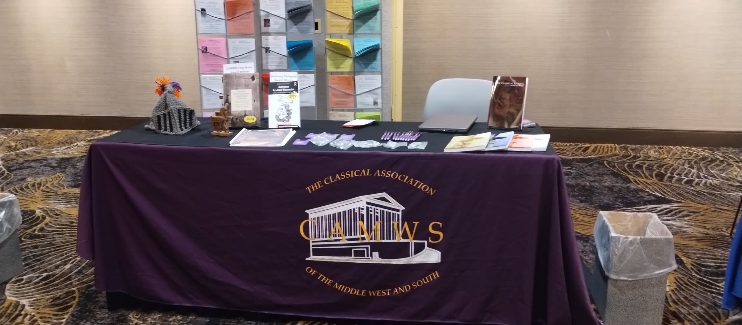 The CAMWS exhibit table draped in purple cloth printed with the association's seal, with brochures and journals on top