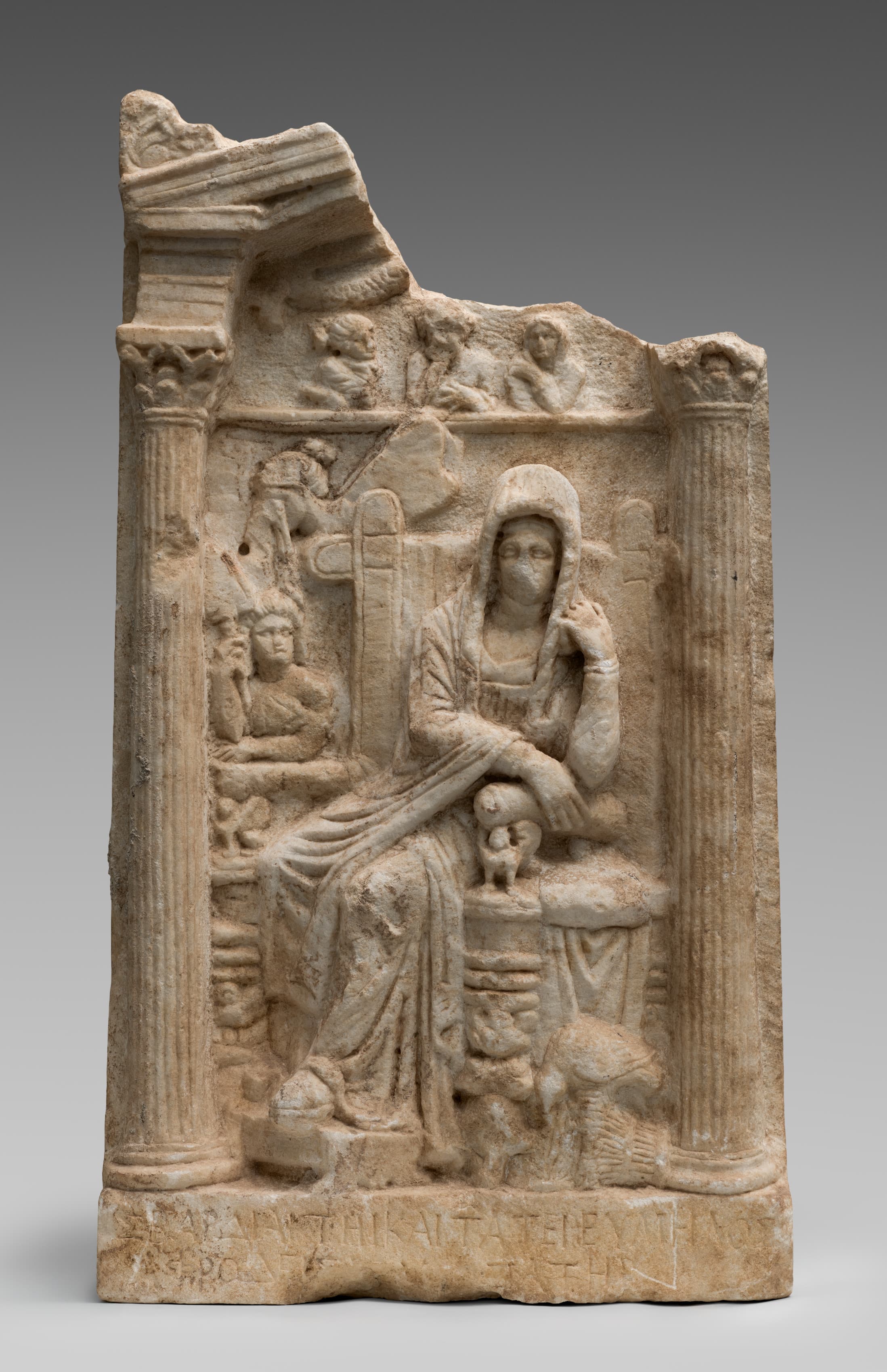 Marble grave relief of a seated woman and her servant girl under an architectural frame, with a Greek dedicatory inscription carved on the base.