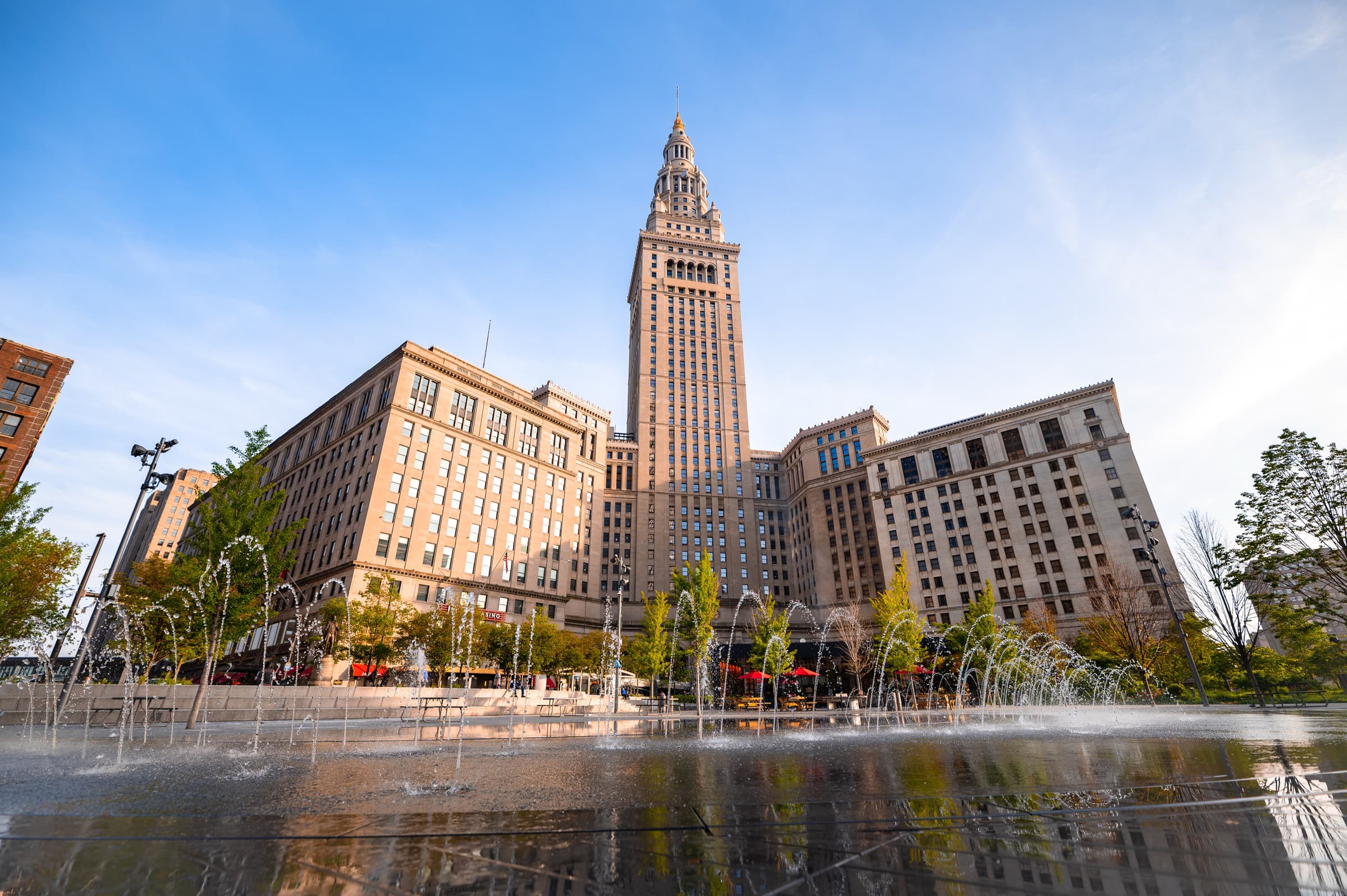 Terminal Tower rising above the Tower City complex behind the fountains of Cleveland's Public Square on a clear day.