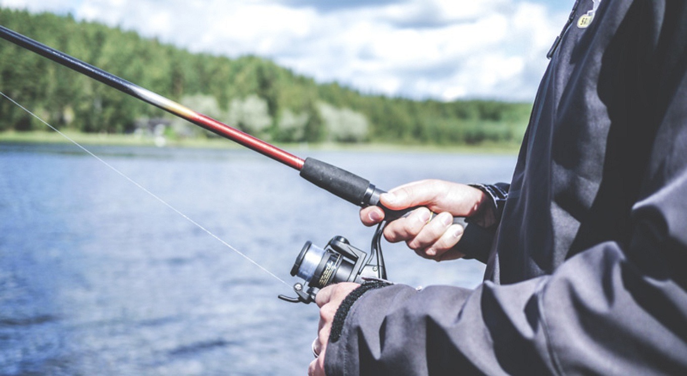 A person fishing from the shore of Carlyle Lake under a partly cloudy summer sky.