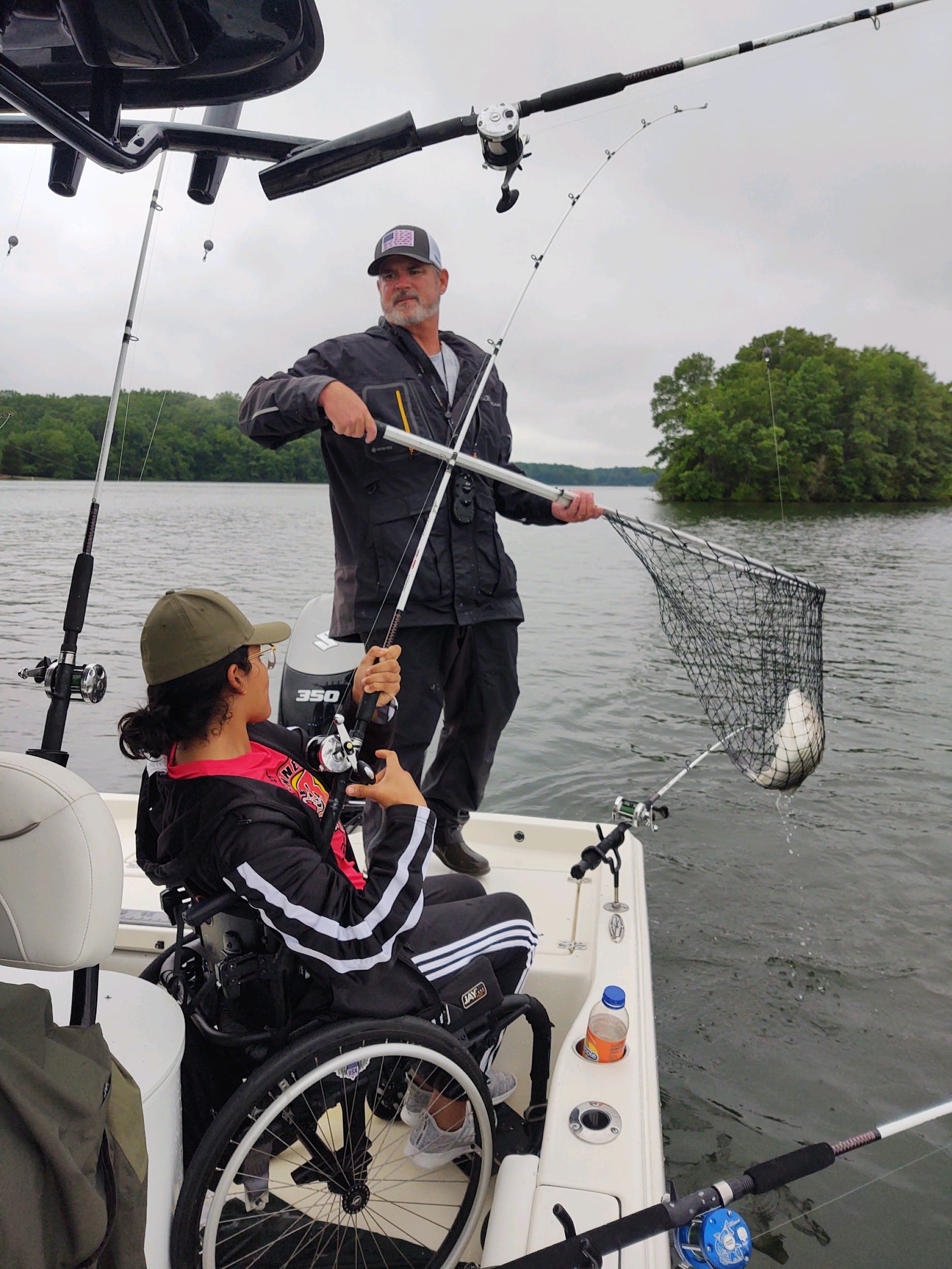Veterans fish together from a boat on a funded outdoor outing, one hoisting a landing net