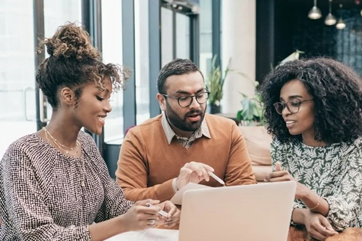 Three people at a table working through paperwork together on a laptop.