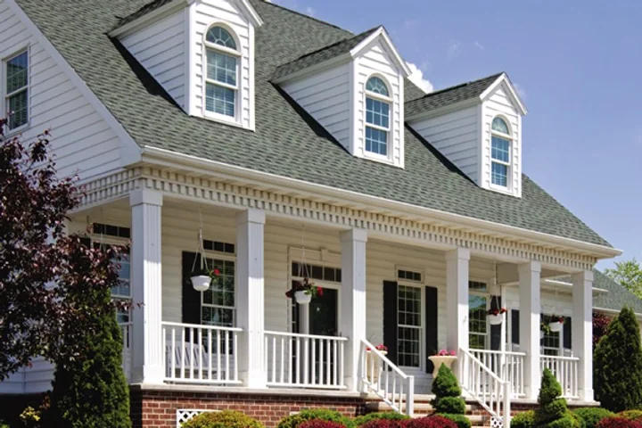 A Connecticut cape with a full front porch, white rails, and planted beds along the walk.