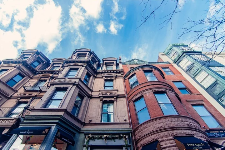 Brick and brownstone rowhouse fronts rising against a bright sky.