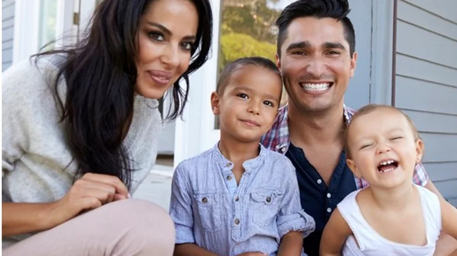 A family of four sitting together on the front steps of their home.