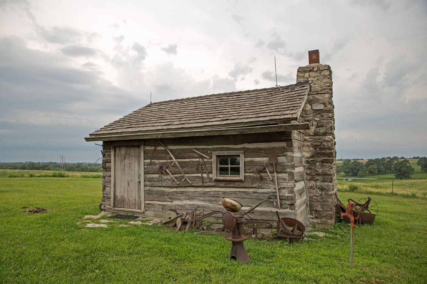 A weathered log cabin with a stone chimney on the farm grounds.