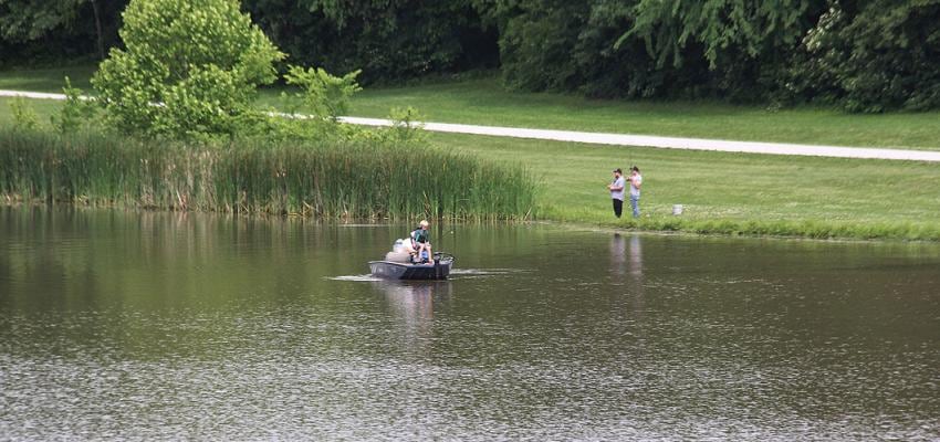 A paddler on the small fishing lake at Rocky Hollow Park, with anglers on the far bank.