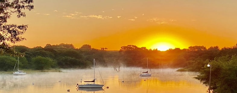 Sailboats on a misty cove at sunrise.