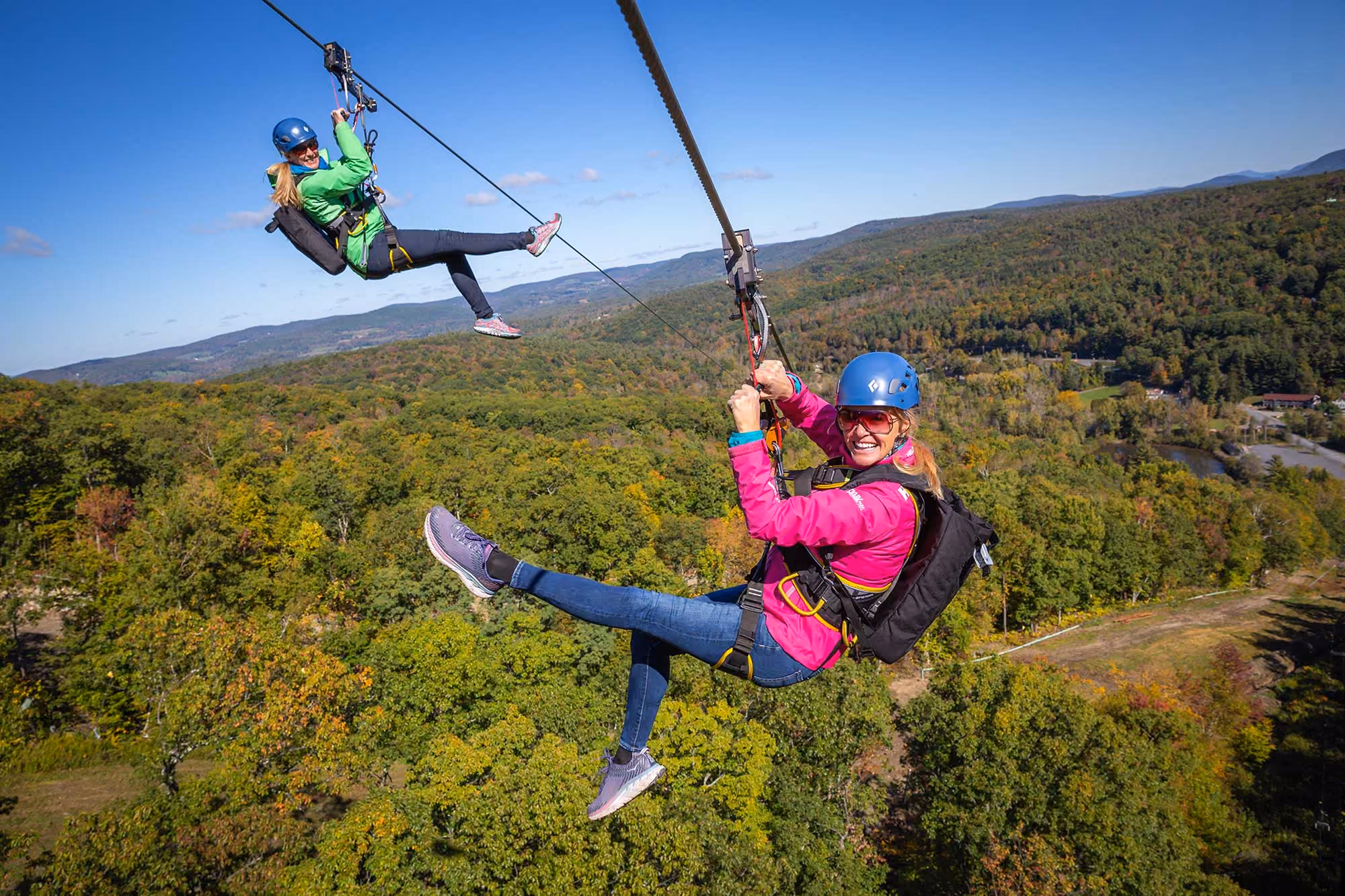 Two riders on the zip line above the autumn forest at Catamount