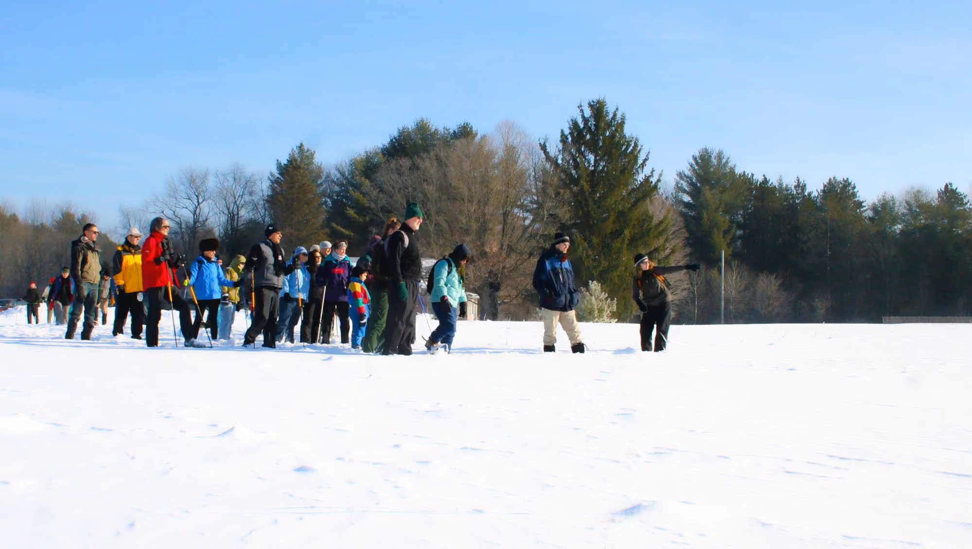 A group snowshoeing across a snowy field under a blue sky