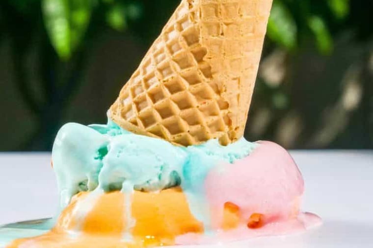 An ice cream cone tipped over into melting scoops of blue and pink ice cream