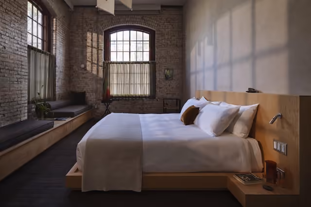A guest room at Pocketbook Hudson, where the former textile mill’s original brick walls and oversized windows have been preserved. Credit: Adrian Gaut