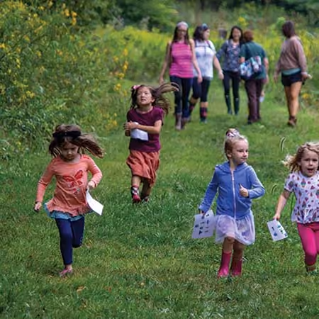 Young children and their parents running down a mown trail through a meadow on an Early Adventures hike