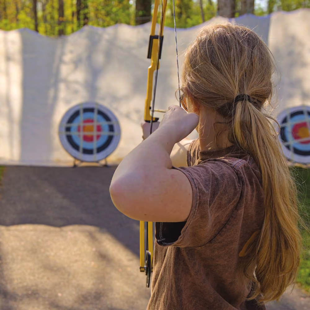 A girl drawing a bow toward an archery target