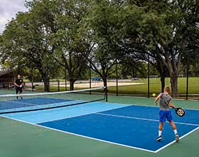 An adult and a child playing on an outdoor pickleball court