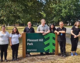 A group of seven people standing behind a green sign that says Pleasant Hill Park.