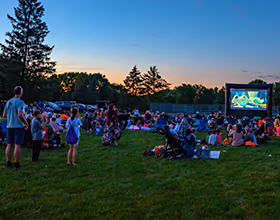 A group of people are watching a movie on an inflatable screen at sunset.