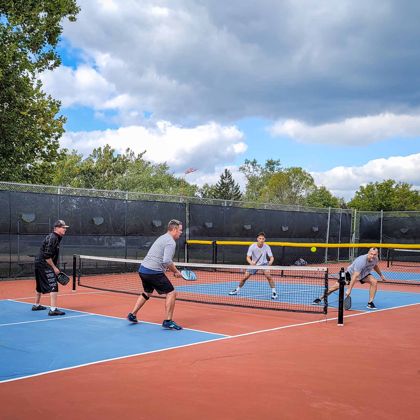 Pickleball players at the net on blue and red courts