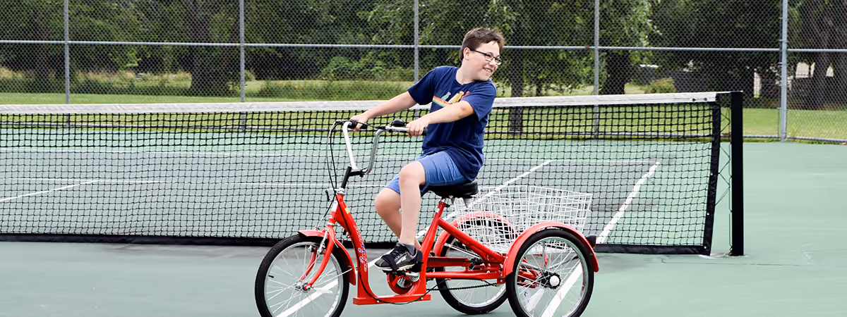 Boy riding adapted bike on tennis court at Oak Grove Park