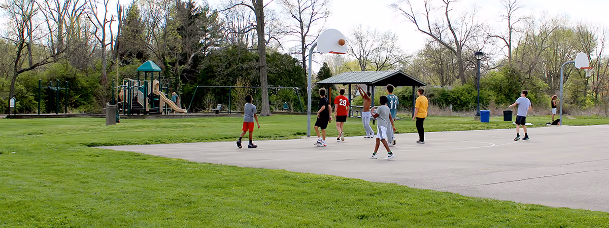 Boys playing basketball at Concept Park, playground and shelter in background.