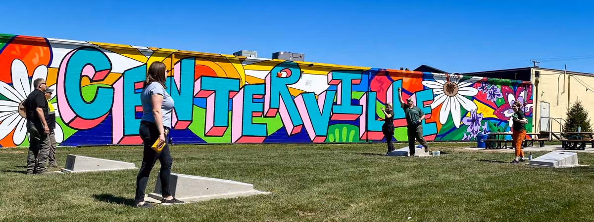 Neighbors playing cornhole in front of the colorful Centerville mural