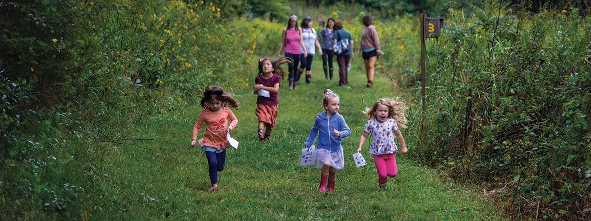 Young children and their parents running down a mown trail through a meadow on an Early Adventures hike