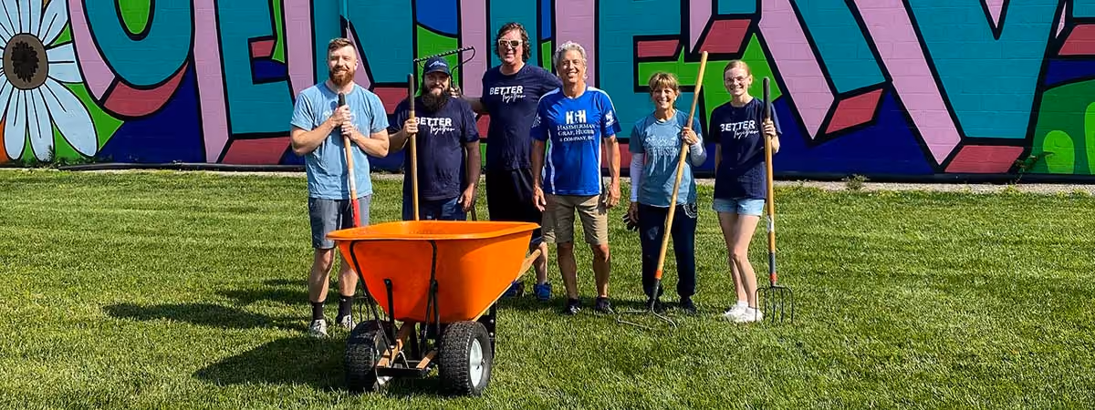 Volunteers with rakes and an orange wheelbarrow after a workday