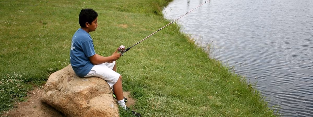 A boy fishing from a rock at the Rosewood Park pond