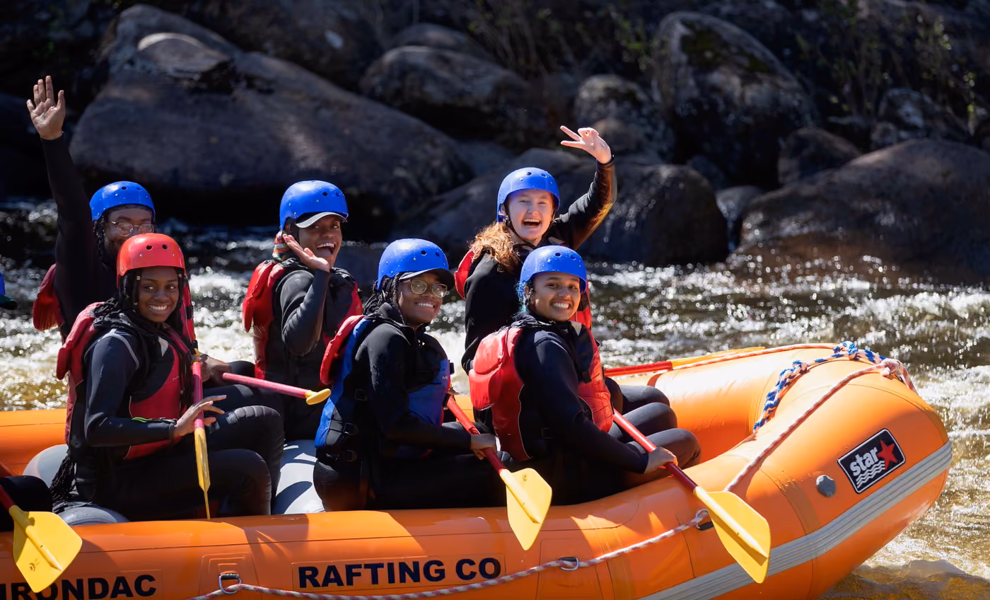 An orange raft full of paddlers waving from the rapids