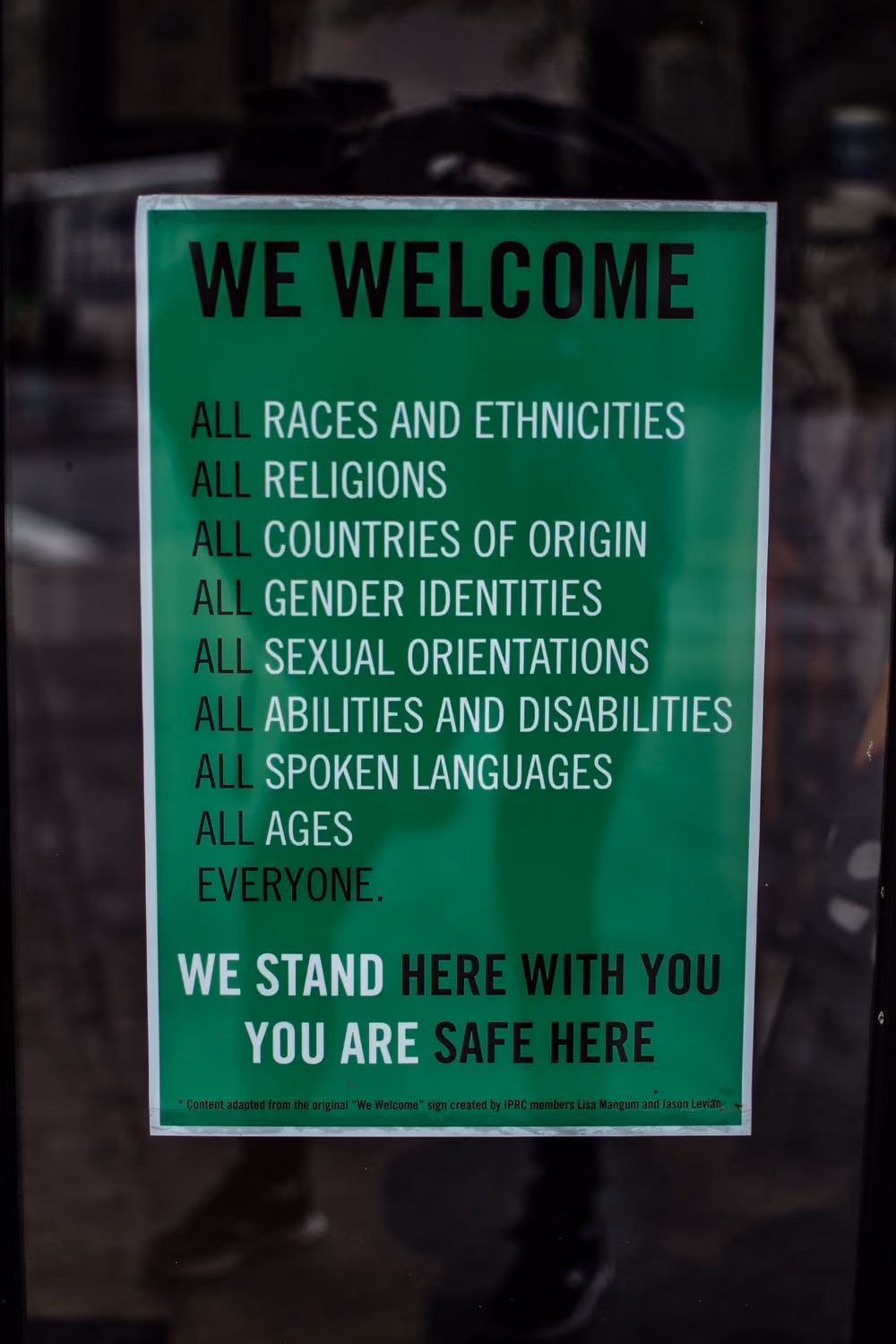 A green We Welcome sign listing all races and ethnicities, religions, countries of origin, gender identities, sexual orientations, abilities and disabilities, spoken languages and ages