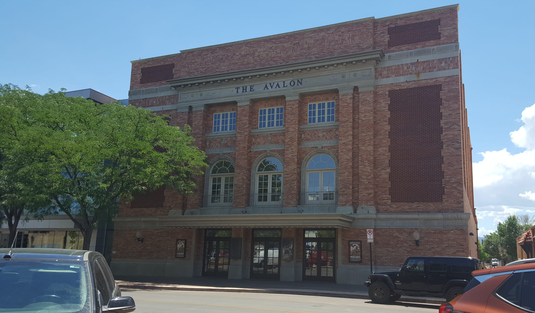 The Avalon Theatre from across Main Street: a brick and stone façade with THE AVALON carved above three arched windows, a canopy over the entrance doors and framed posters either side of them