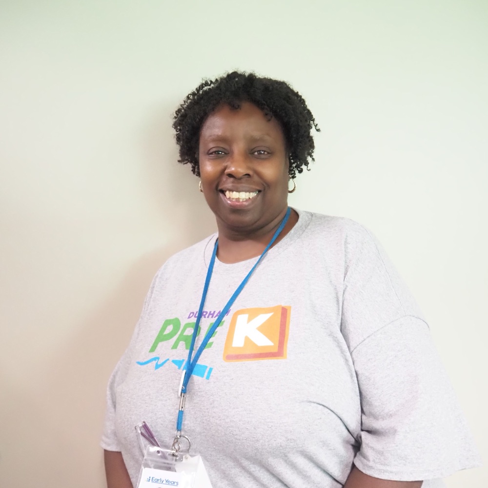 A smiling Durham PreK staff member in a Durham PreK shirt and Early Years lanyard at a program site