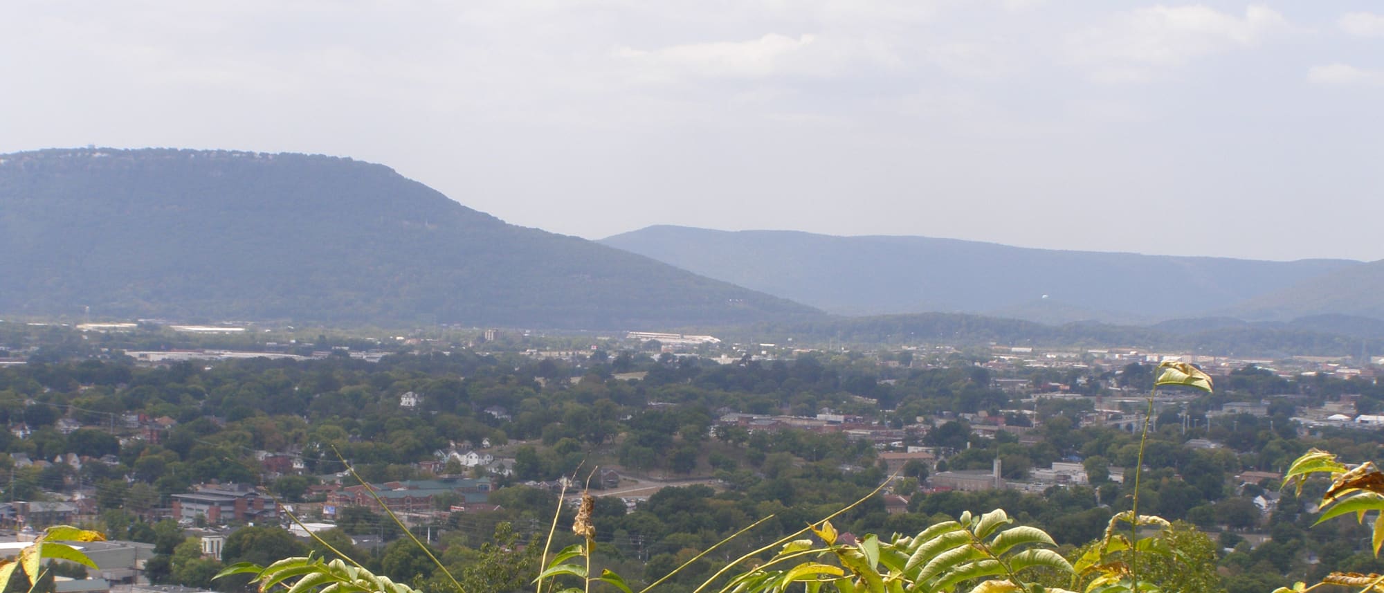 The long wooded profile of Lookout Mountain across the horizon, with the floor of the Chattanooga basin below it — houses, trees, warehouses and a scatter of taller buildings receding into haze.