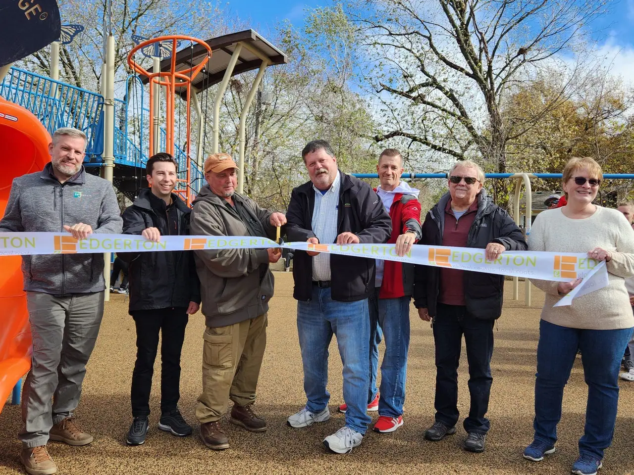 Residents and City officials hold a ribbon in front of the new orange slides at Glendell Acres Park.