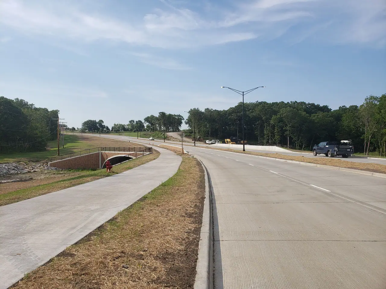 A new four-lane concrete road with a trail and streetlights over Bull Creek.