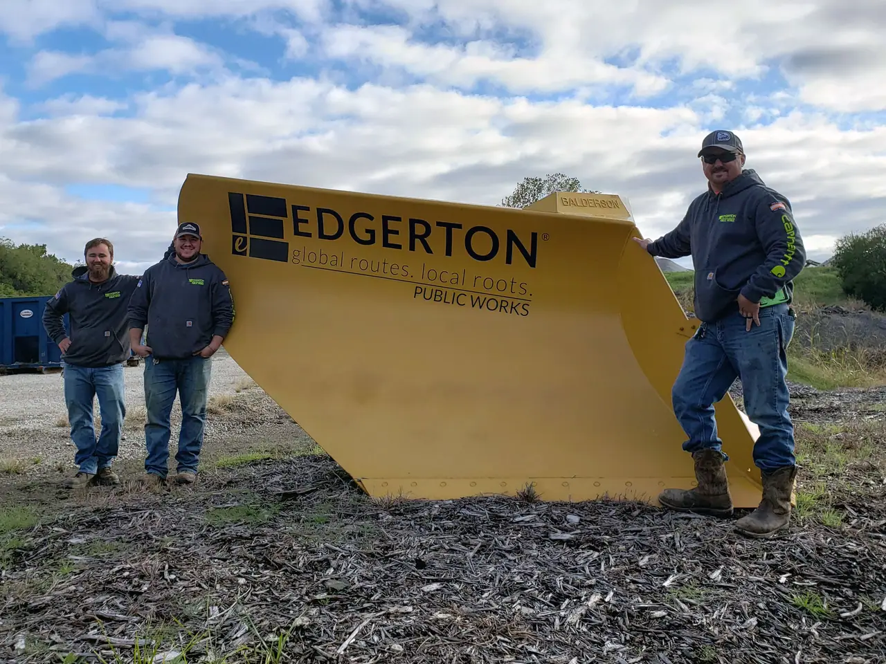 Three Public Works employees stand by the monument sign in front of the Public Works facility.