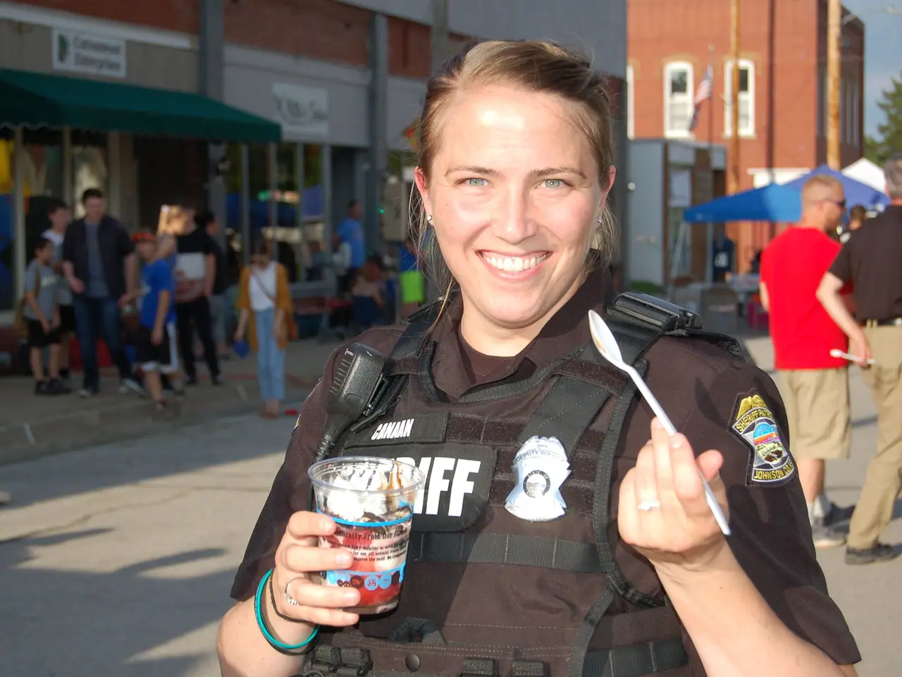 A smiling Sheriff's deputy holds up a snow cone at the Summer Kickoff block party on Nelson Street.