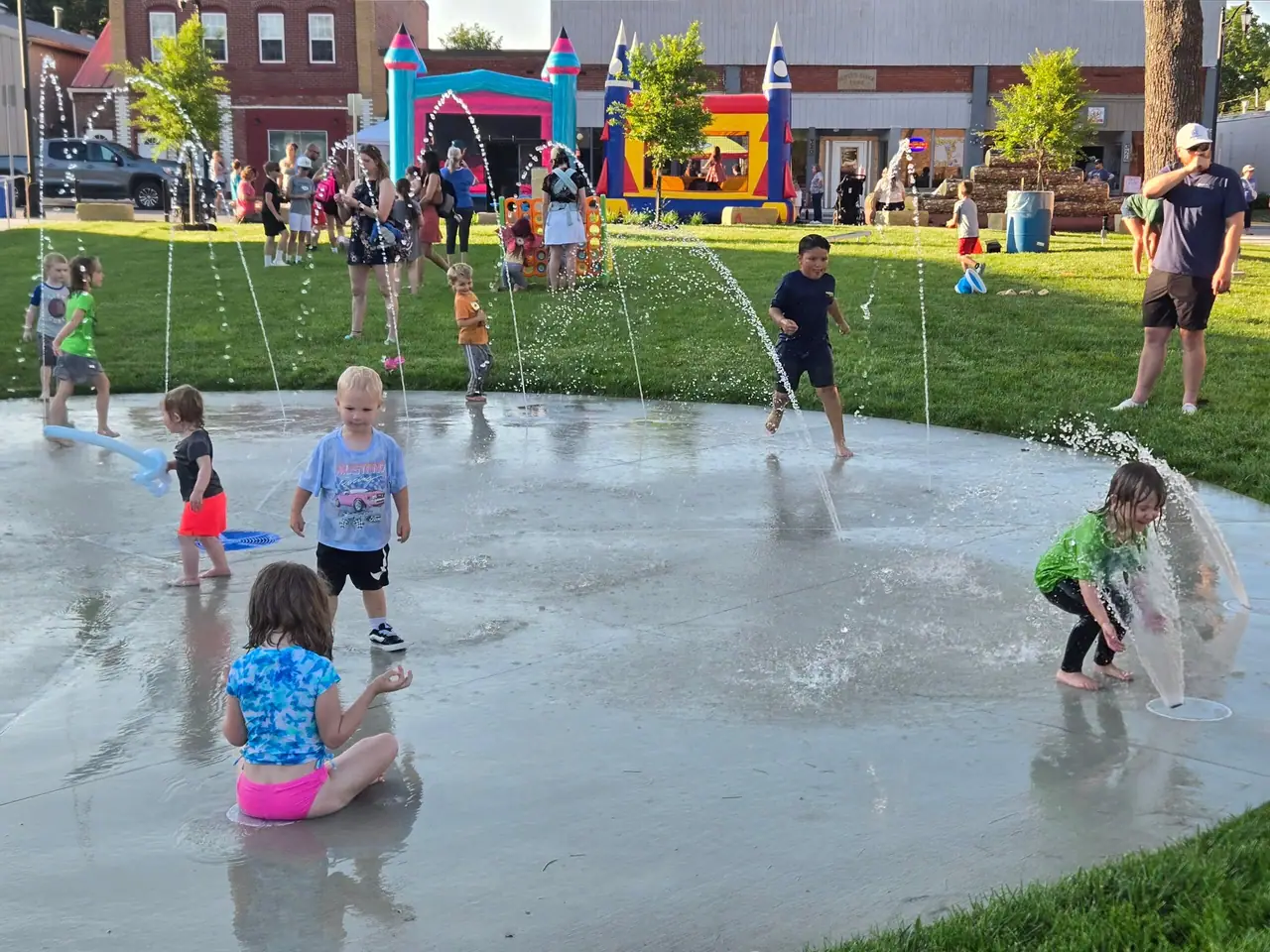 Children play in the splashpad's water jets outside The Greenspace on a summer evening.