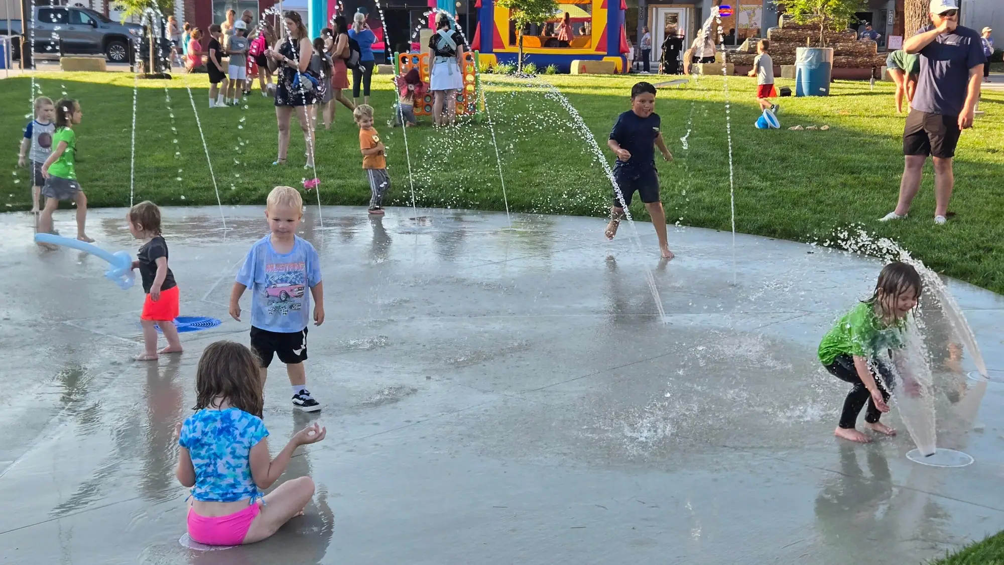Children play in the splashpad's water jets outside The Greenspace on a summer evening.
