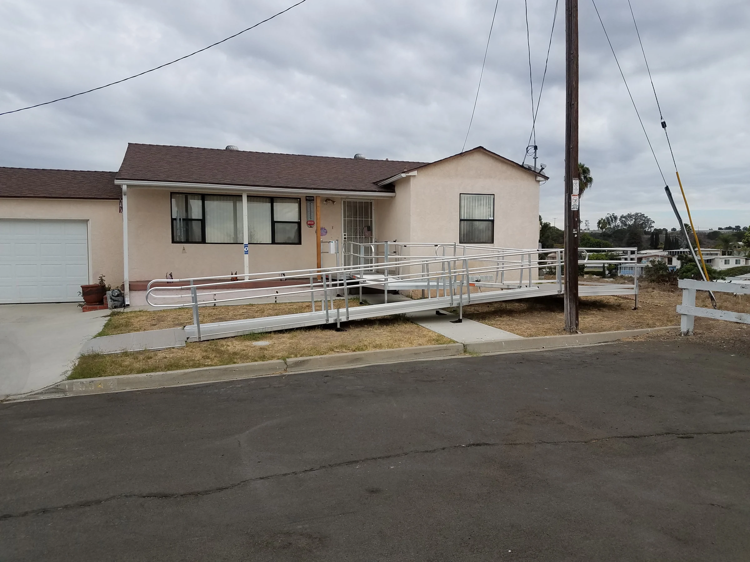 A ramp with handrails leads from the sidewalk to the front door of a single-story home.