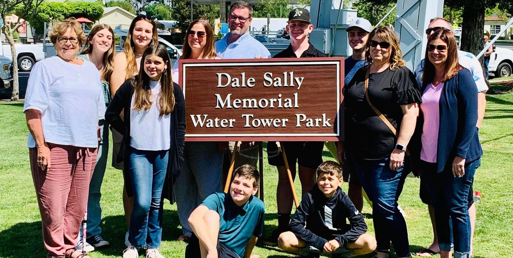 Families and City staff gathered around the new Dale Sally Memorial Water Tower Park sign on dedication day.