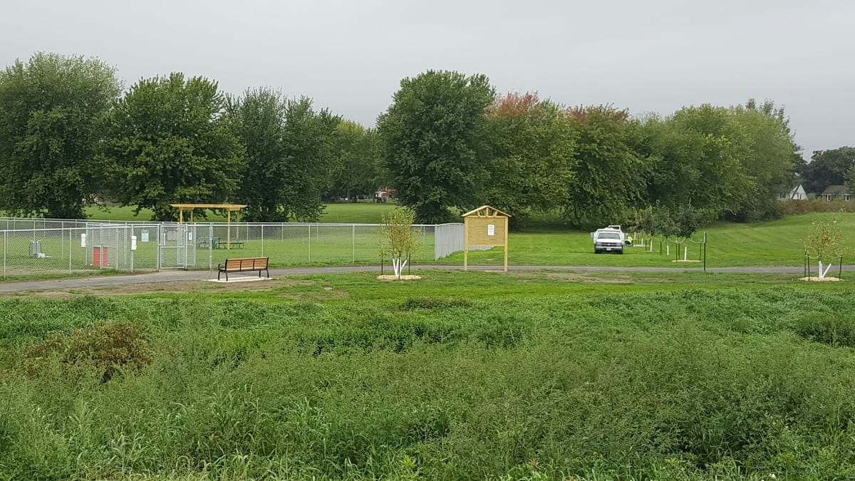 The fenced Fairmont dog park with its gate, sign, and shelter, seen across the adjoining field
