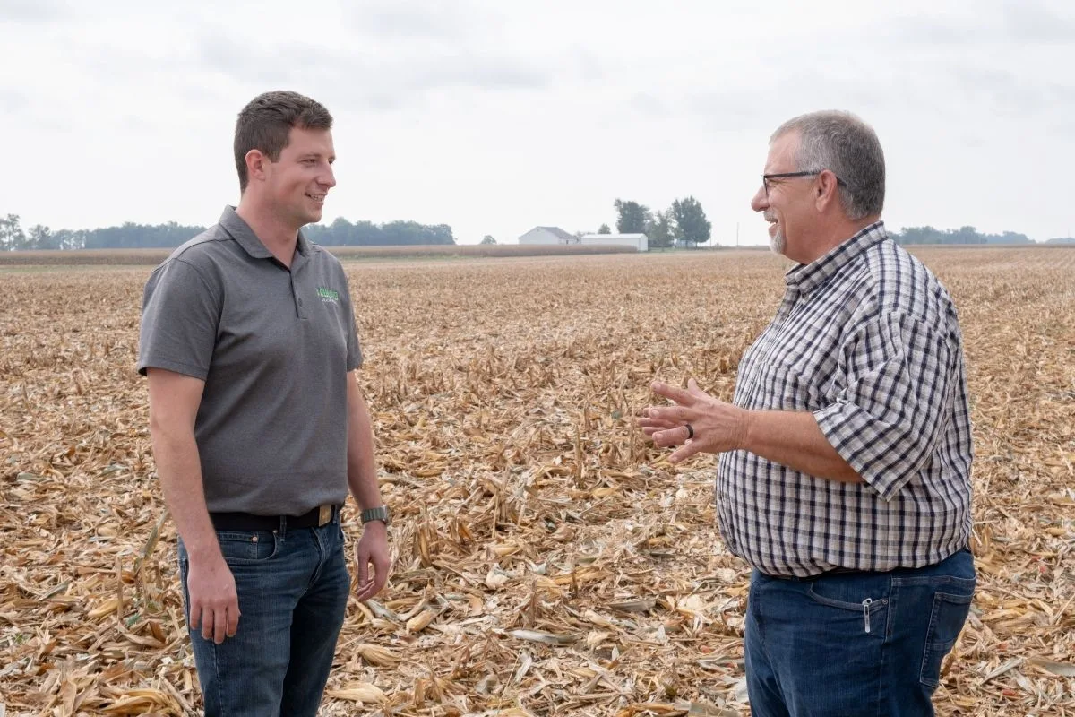 Rodney Rulon and Austin Conrad talk face to face in a harvested cornfield.