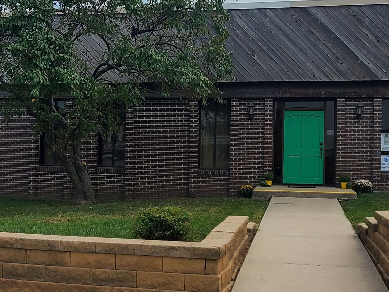 The front walk and green door of the GHRPC office, framed by brick planters and a small tree.