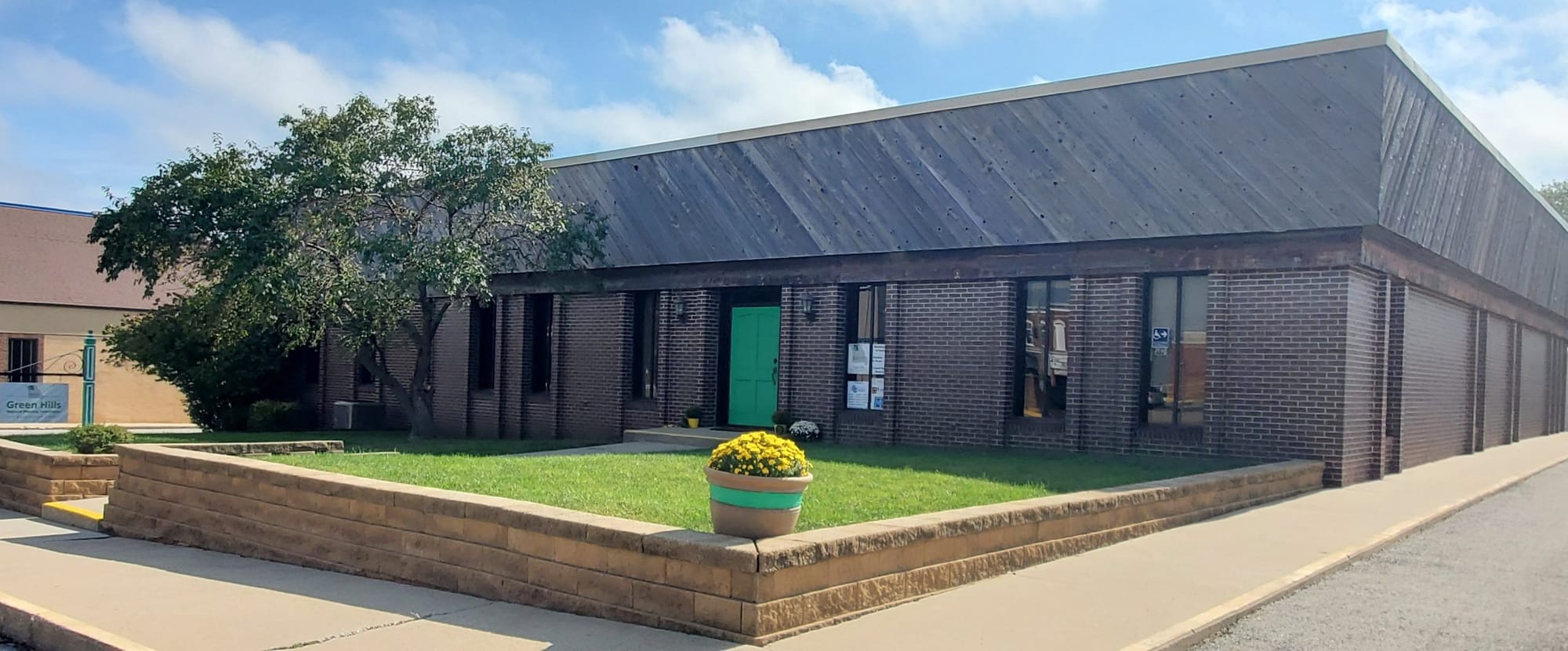 The Green Hills Regional Planning Commission office, a long low brick building with a green door and a planter of yellow mums out front.