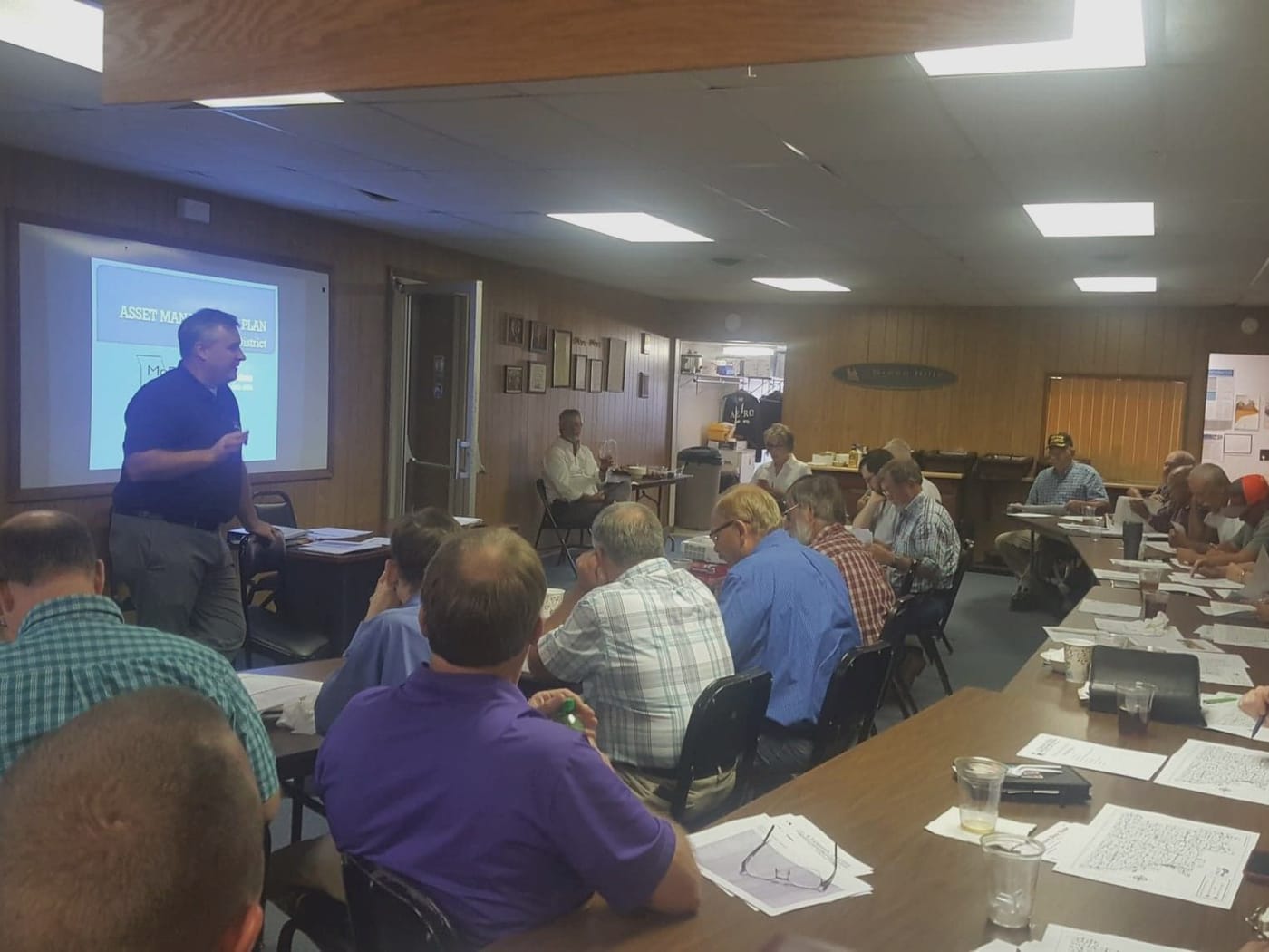 A speaker presents slides to a room of local officials seated around tables at a Transportation Advisory Committee meeting.
