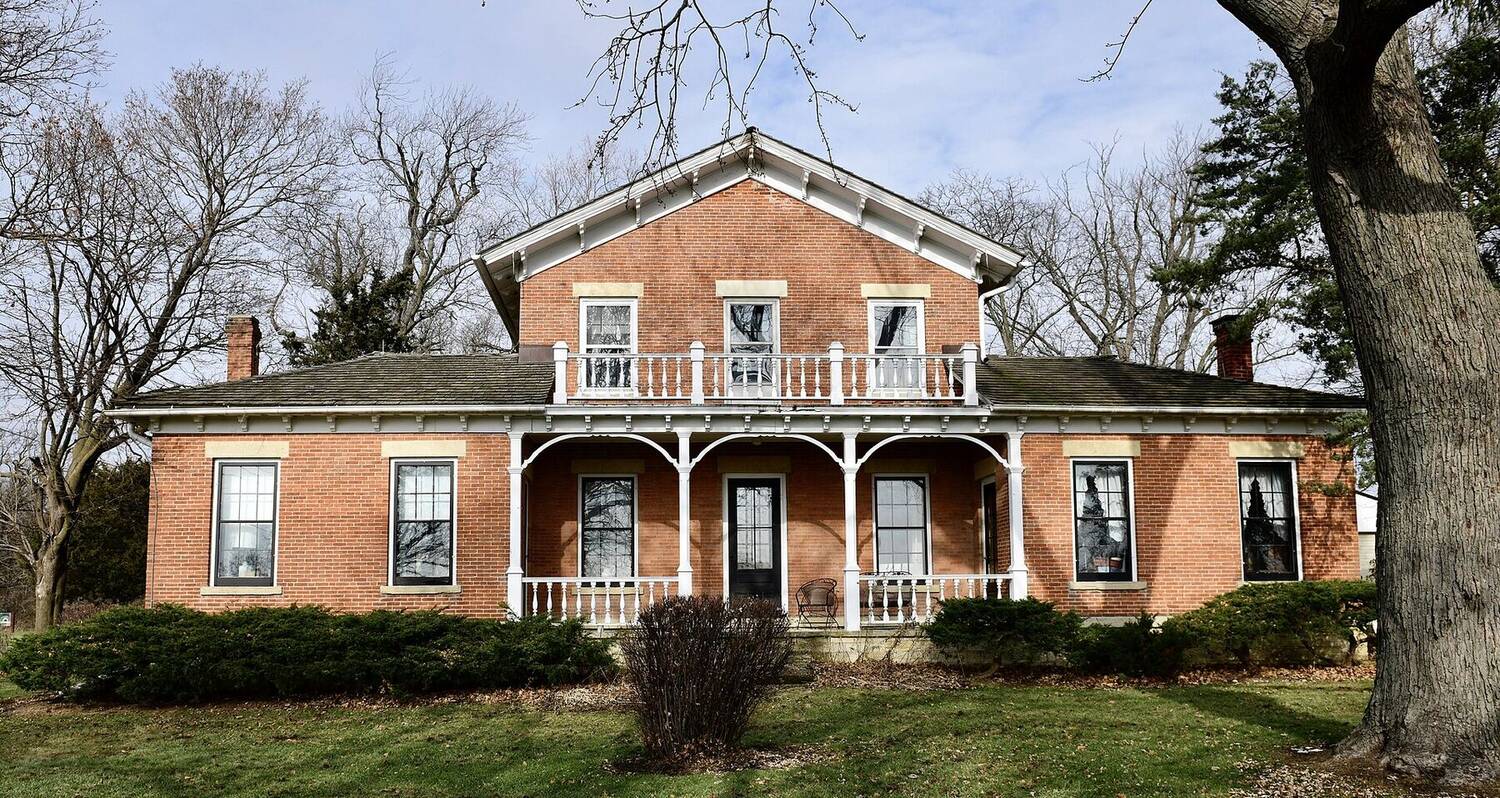 A two-story 19th-century red brick farmhouse with a white porch, in Kane County, Illinois.