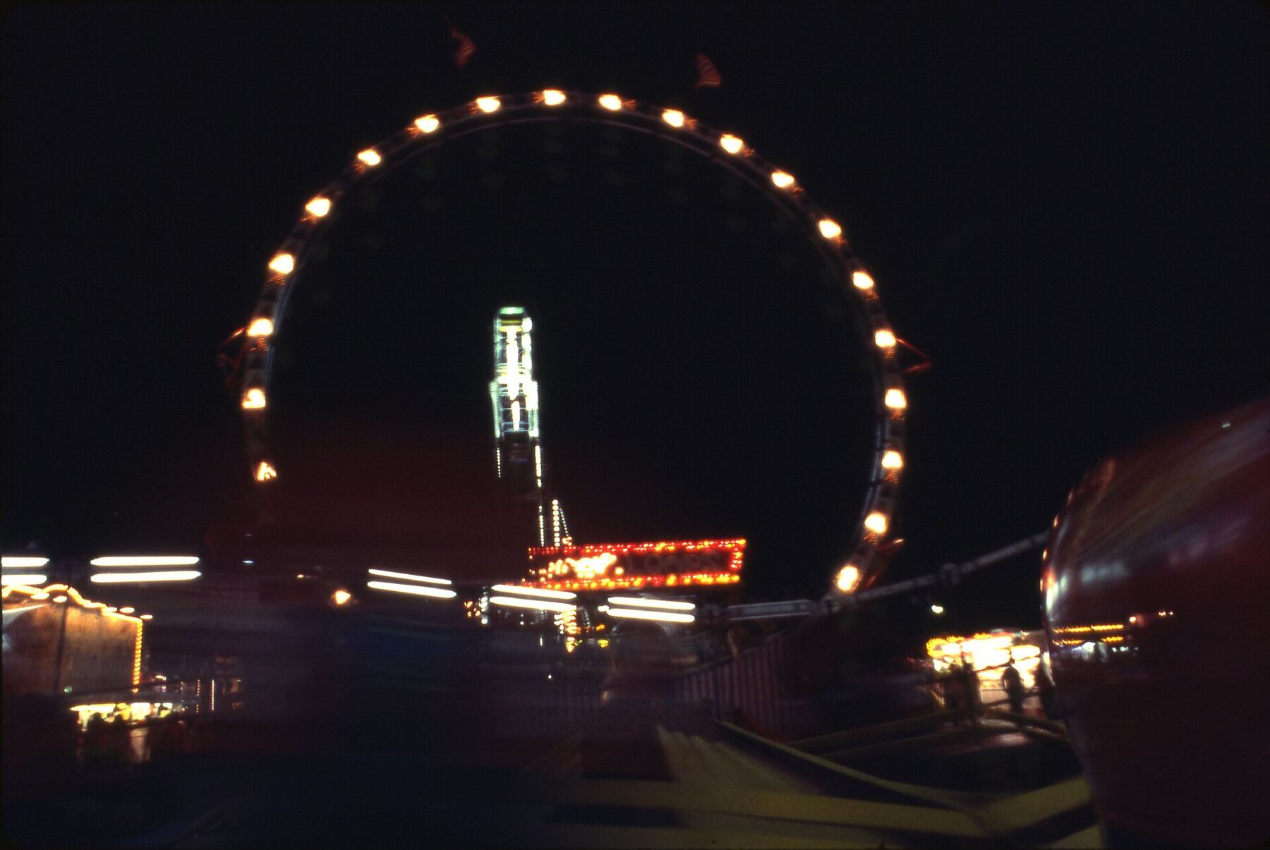 A lit ferris wheel and carnival rides glowing against a night sky.